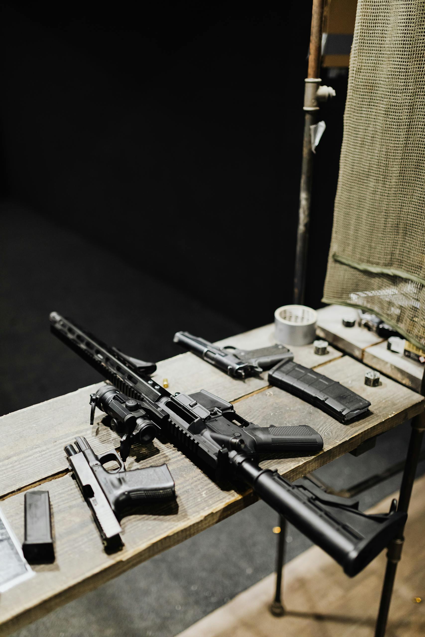 Assorted firearms arranged on a wooden table in an indoor shooting range setting.